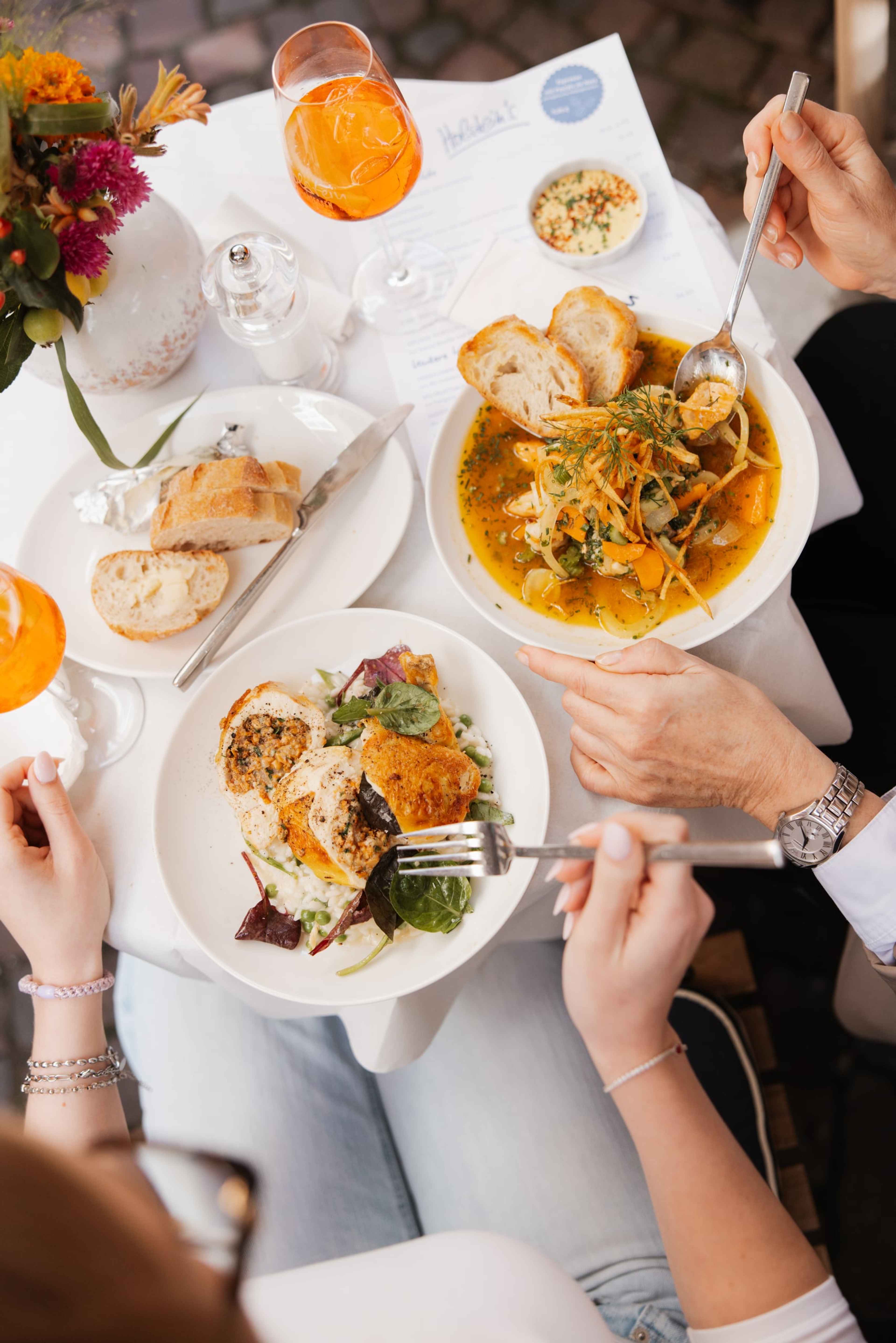 Gedeckter Tisch von oben mit Bouillabaisse, gefülltem Hähnchen auf Reis, Brot, Spritz und einem Blumenstrauß