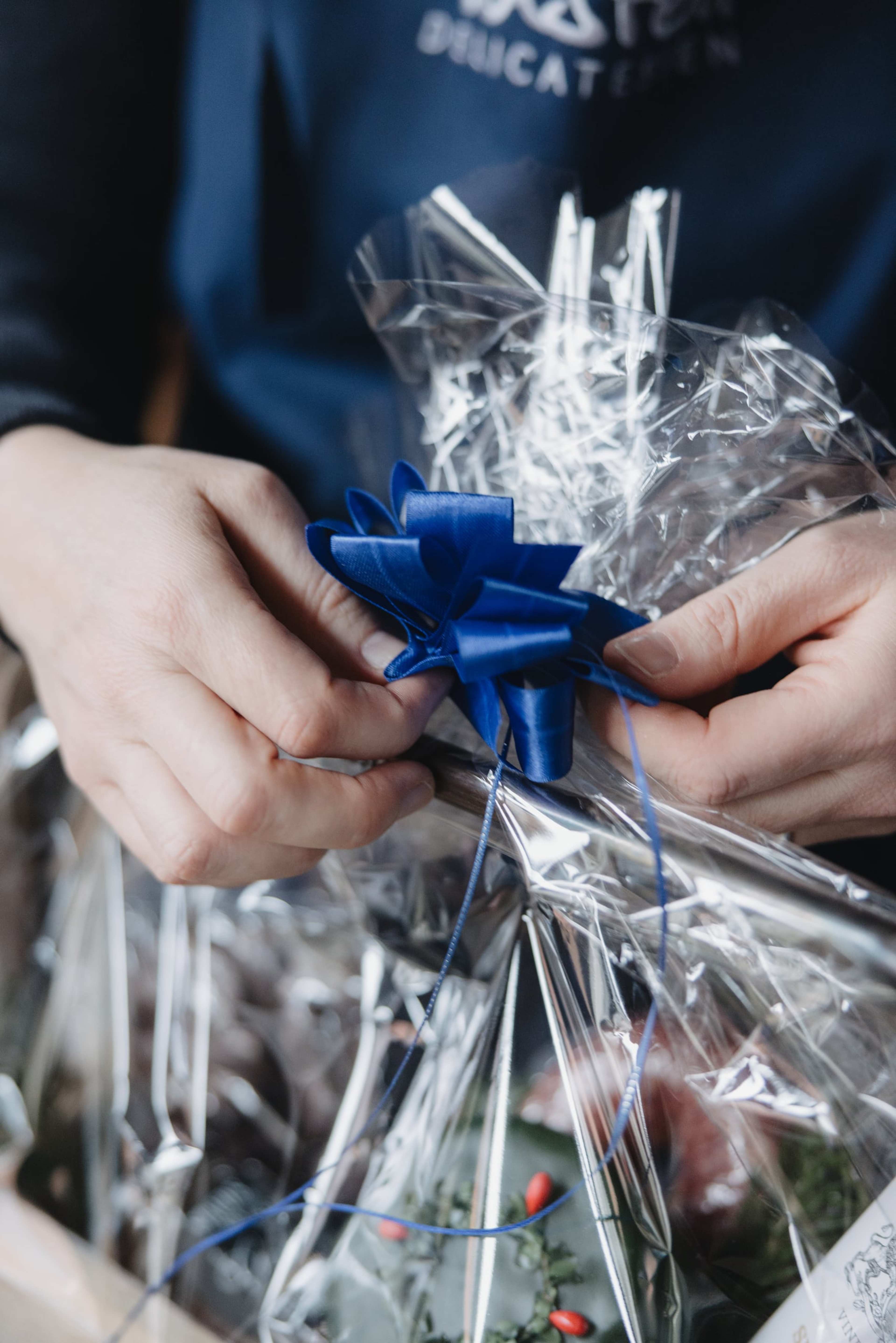 Hände binden eine blaue Schleife an ein in Folie gepacktes Präsent