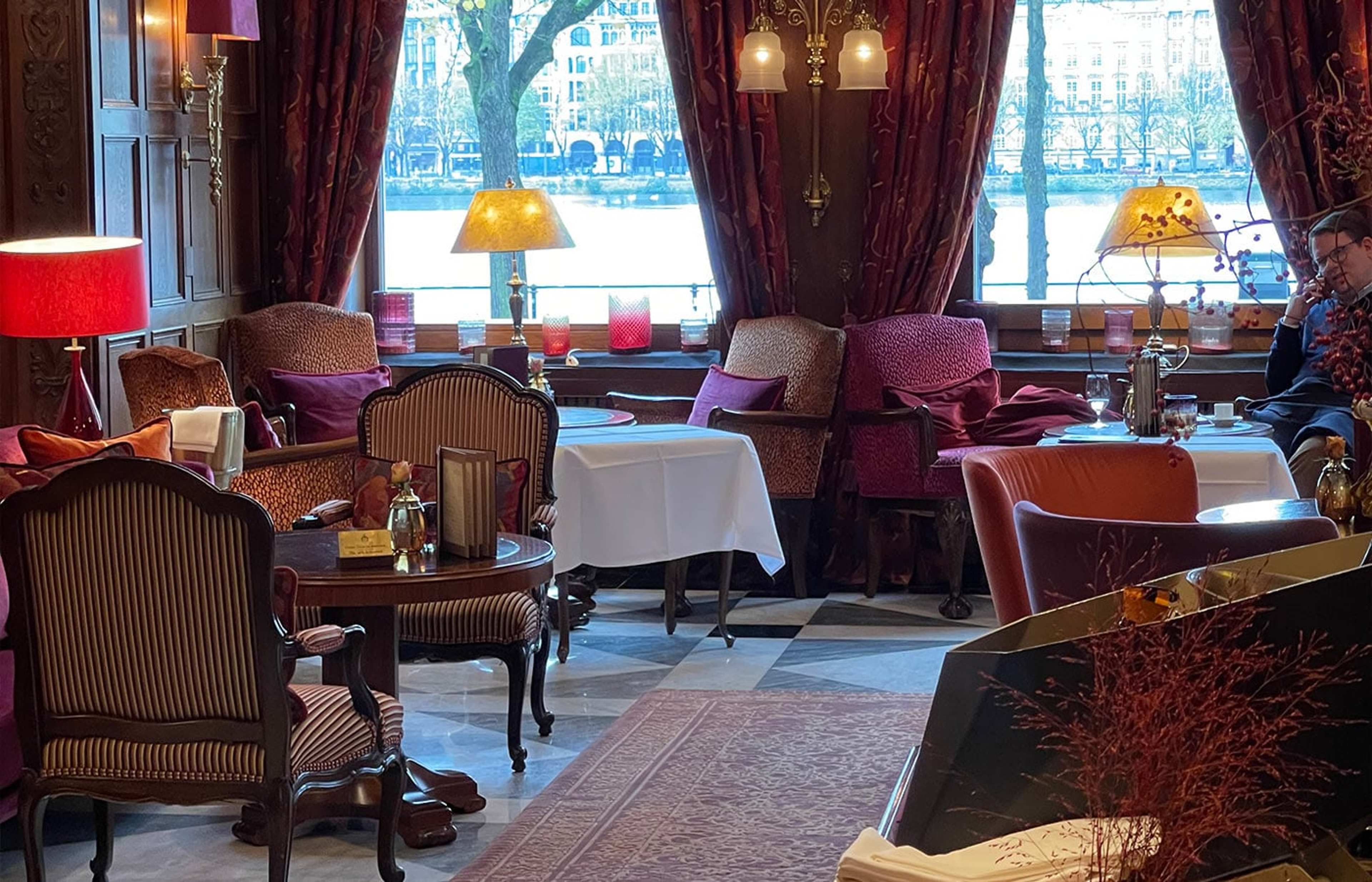 Salon mit Samtsesseln, roten Vorhängen und Blick auf einen See
