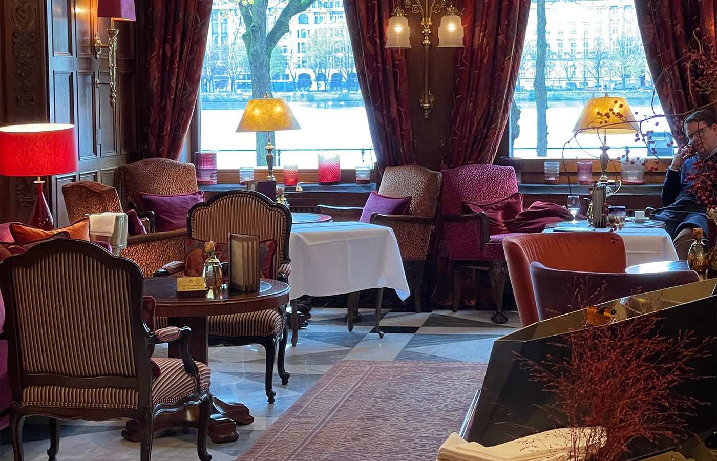 Salon mit Samtsesseln, roten Vorhängen und Blick auf einen See