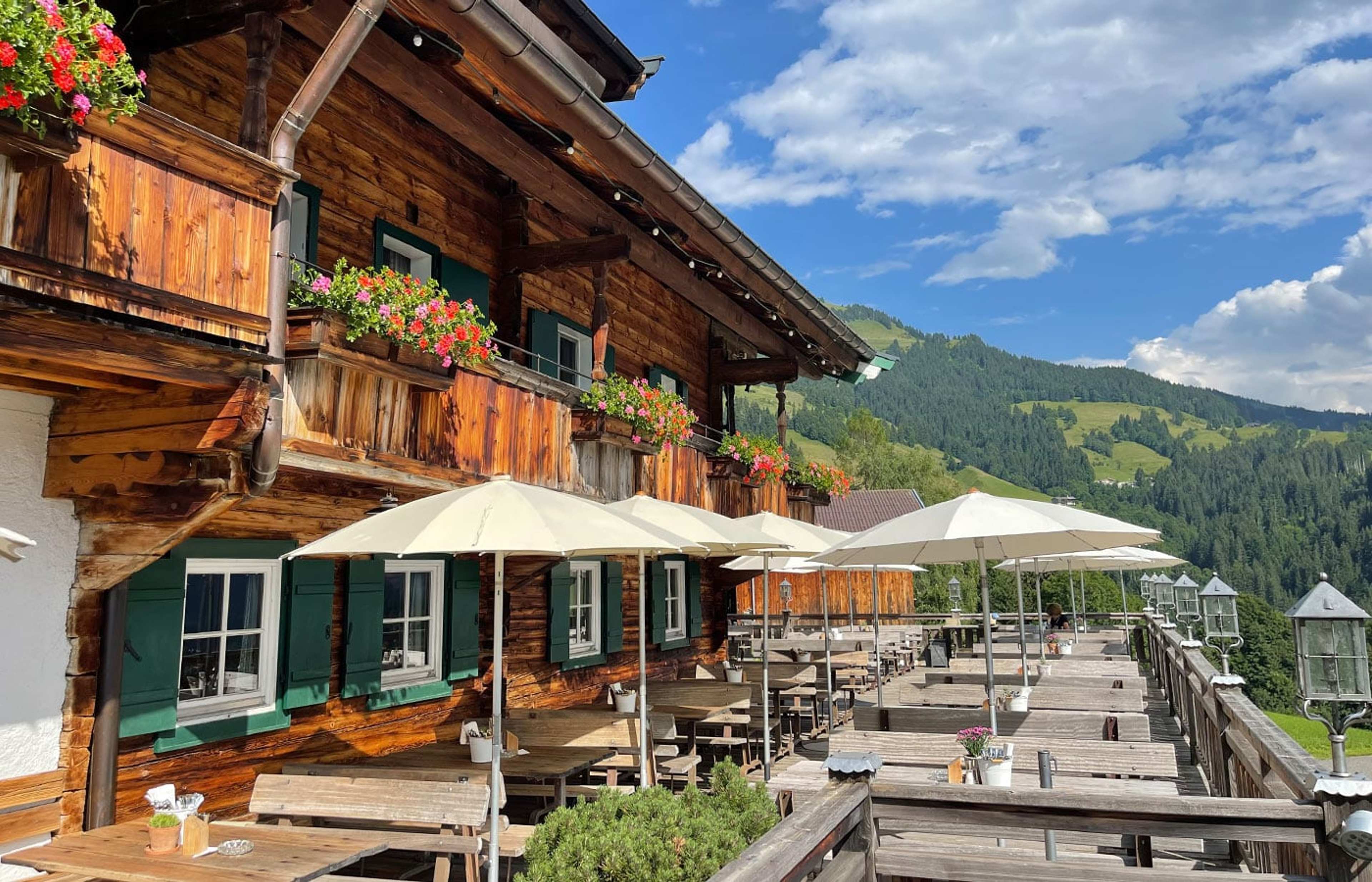 Holzhaus mit Blumenbalkonen und langer Terrasse vor grünen Hügeln