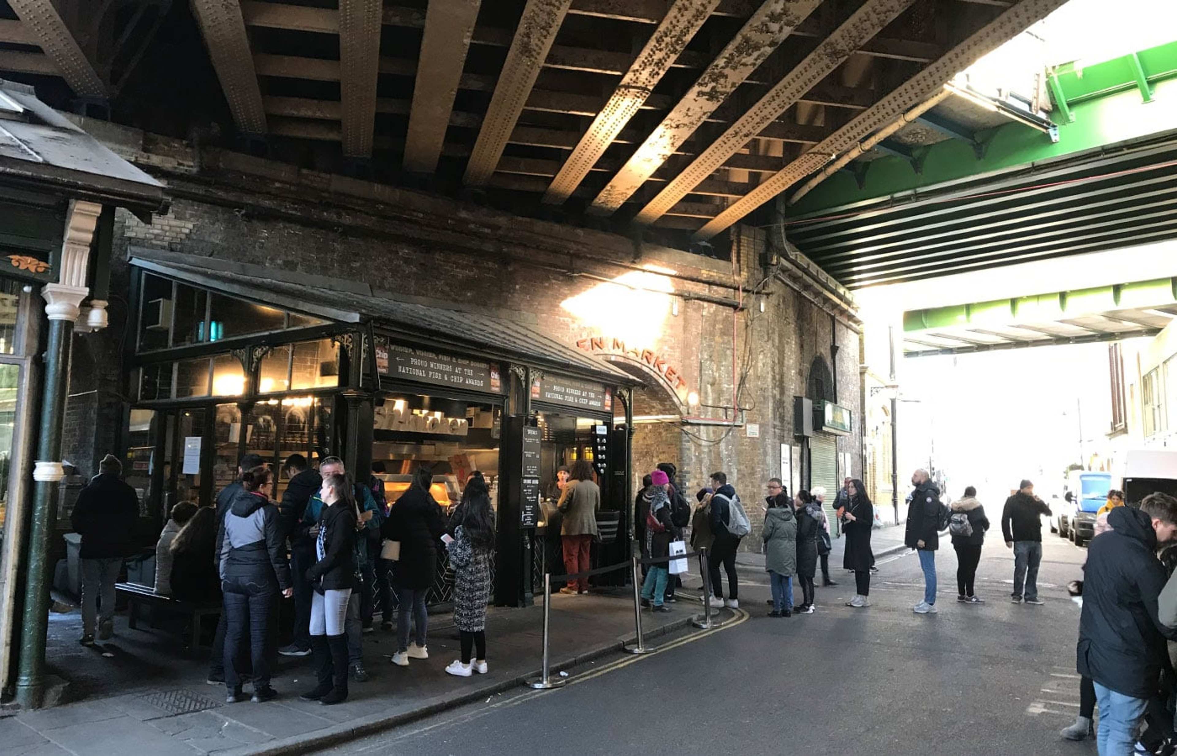 Menschen vor Marktständen unter einer Eisenbahnbrücke