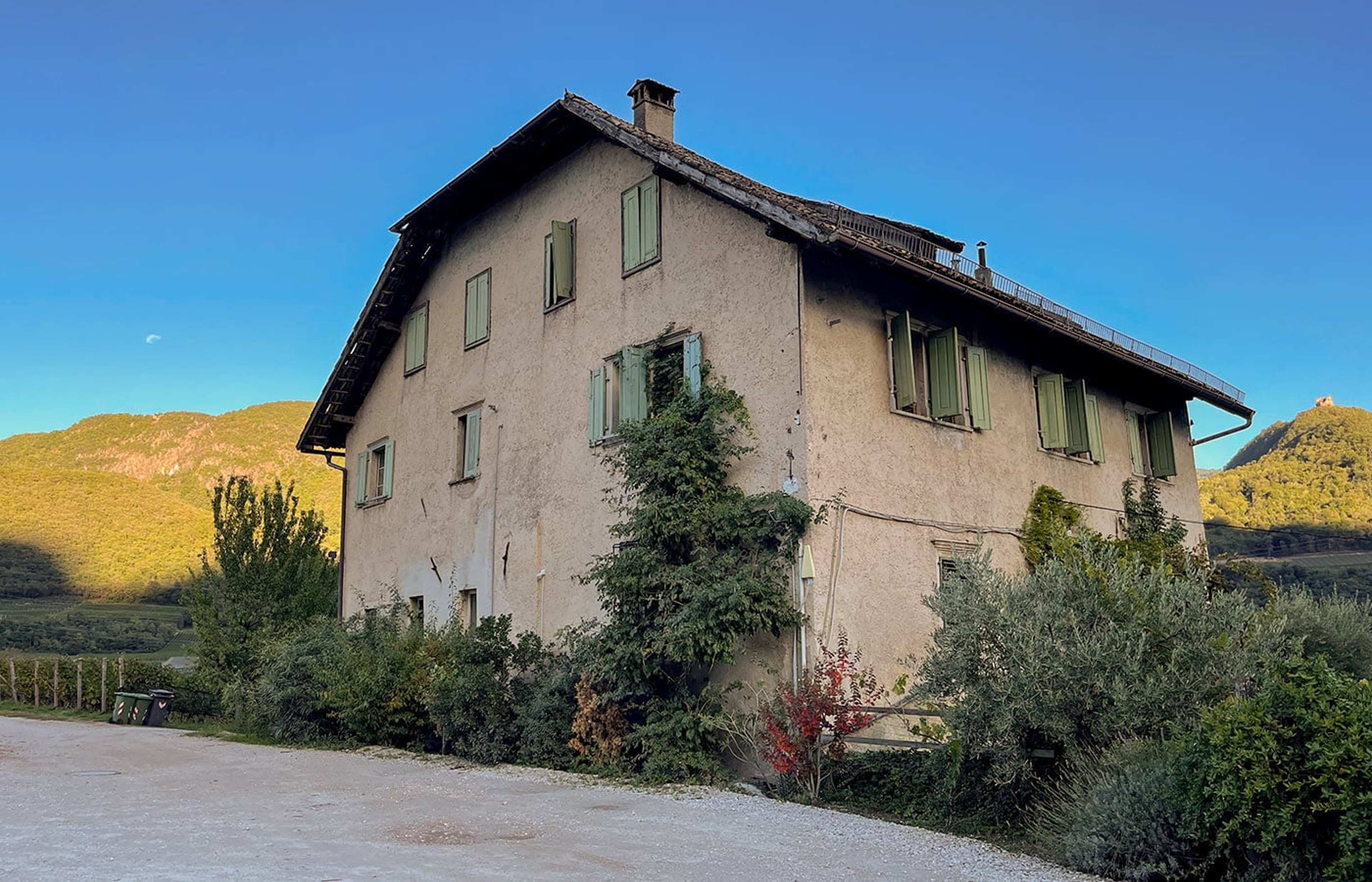Altes Steinhaus mit Fensterläden im Abendlicht vor Bergen