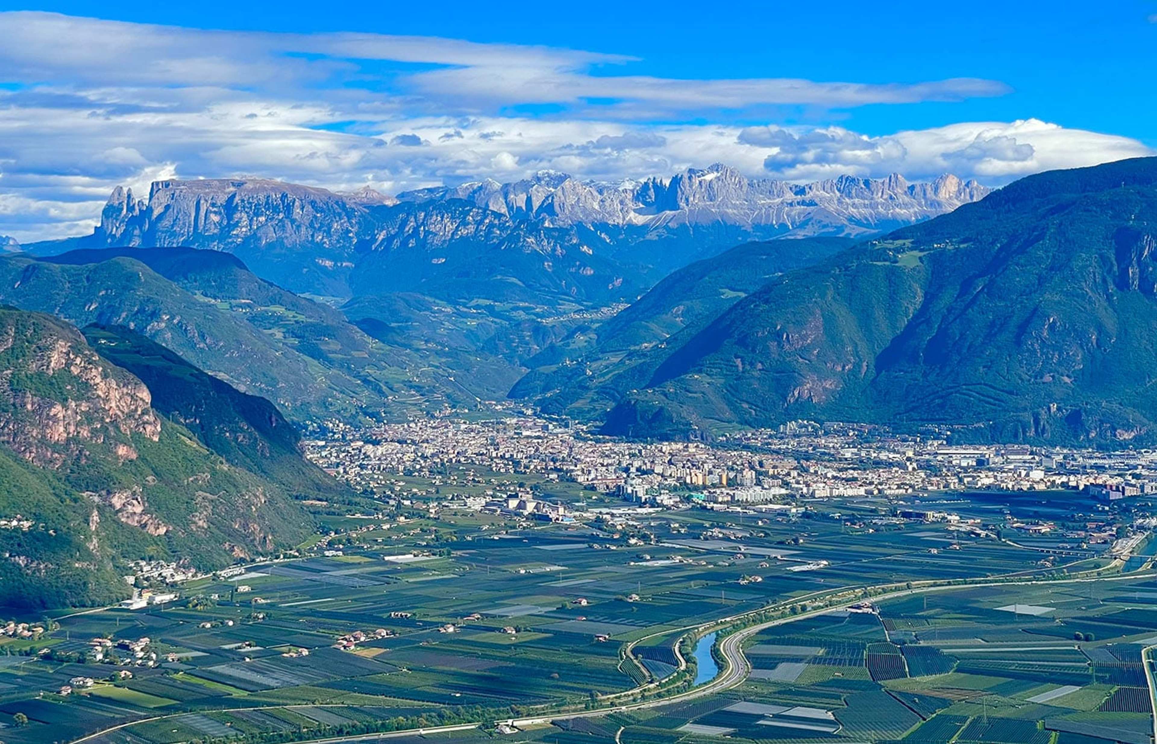 Blick von oben auf ein weites Tal mit Stadt, dahinter Felsgipfel