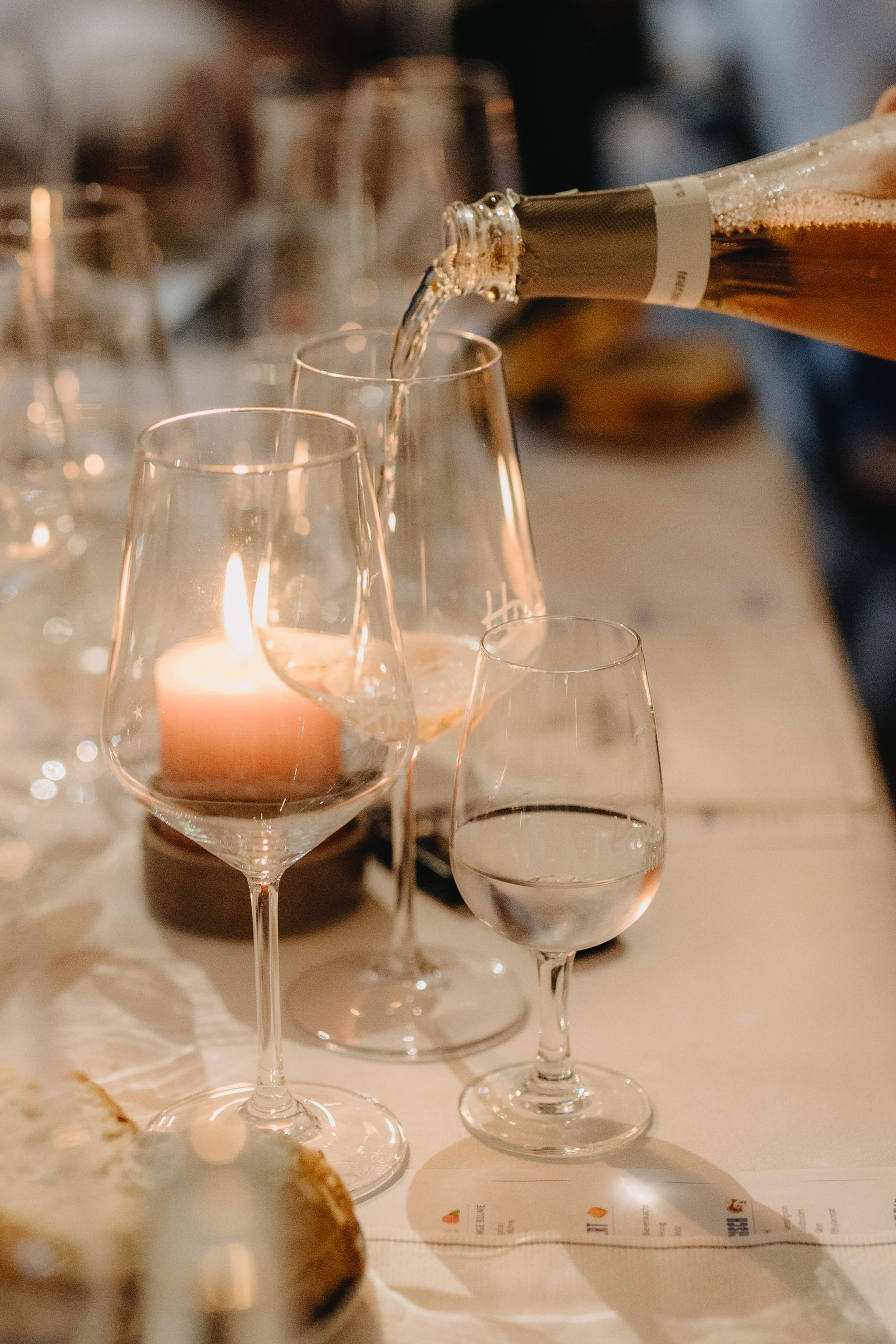 Sekt wird in ein Glas eingeschenkt, davor ein Teelicht und Weingläser auf einem gedeckten Tisch