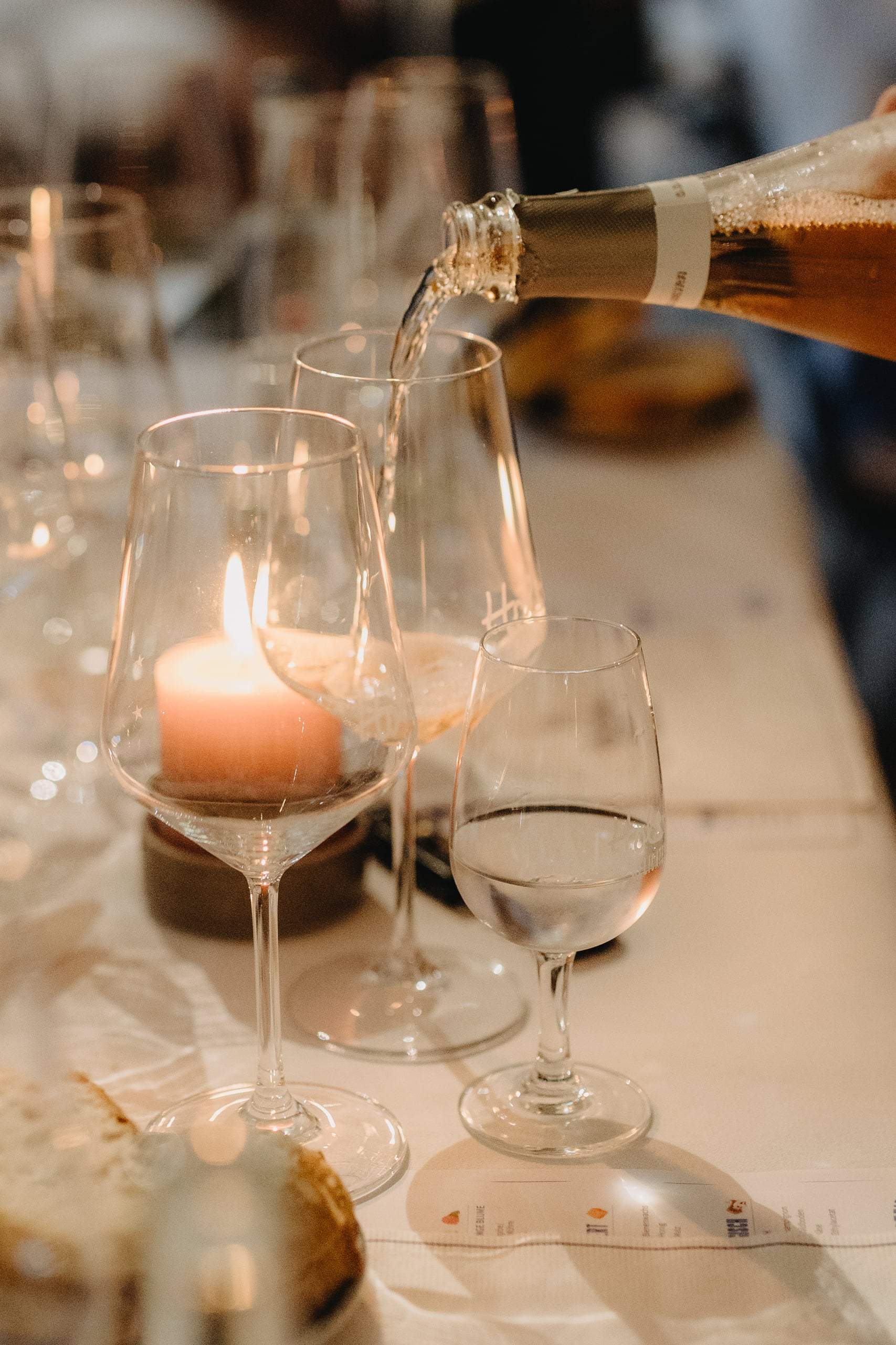 Sekt wird in ein Glas eingeschenkt, davor ein Teelicht und Weingläser auf einem gedeckten Tisch