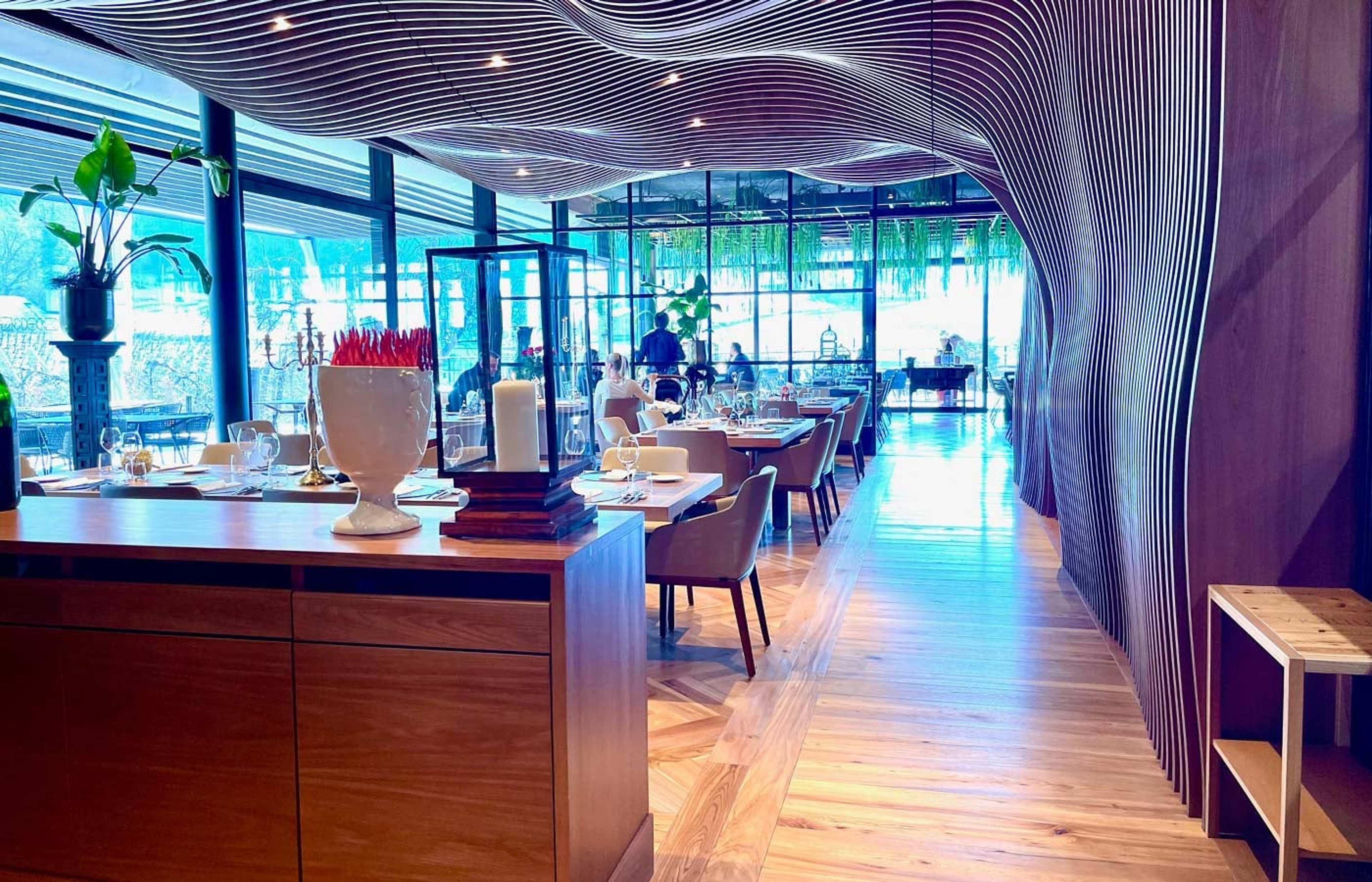 Restaurant mit geschwungener Holzlamellen-Decke und großen Fenstern