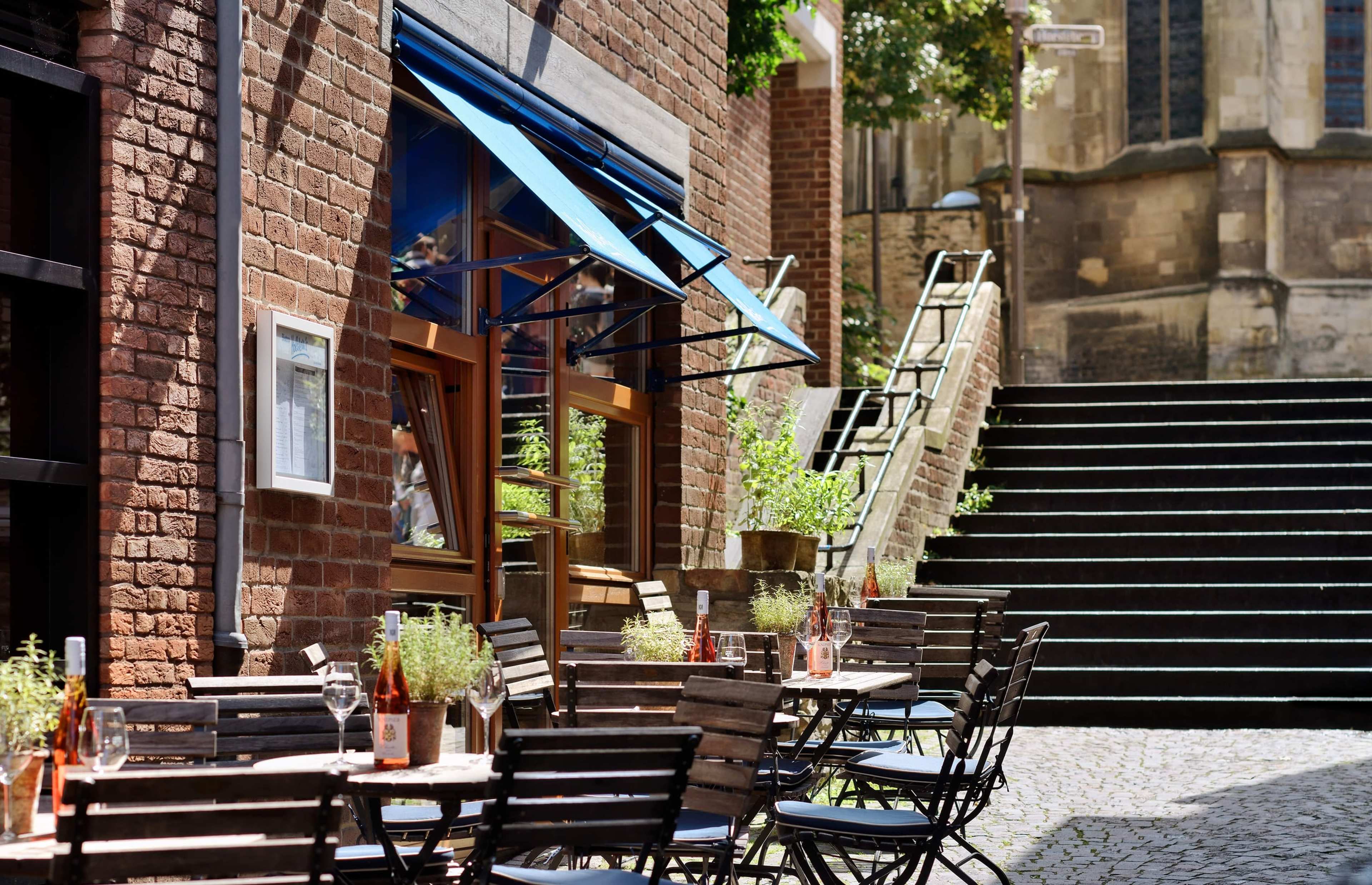 Holstein's Bistro am Dom mit blauen Markisen und Terrasse, daneben Stufen hinauf zur Kirche