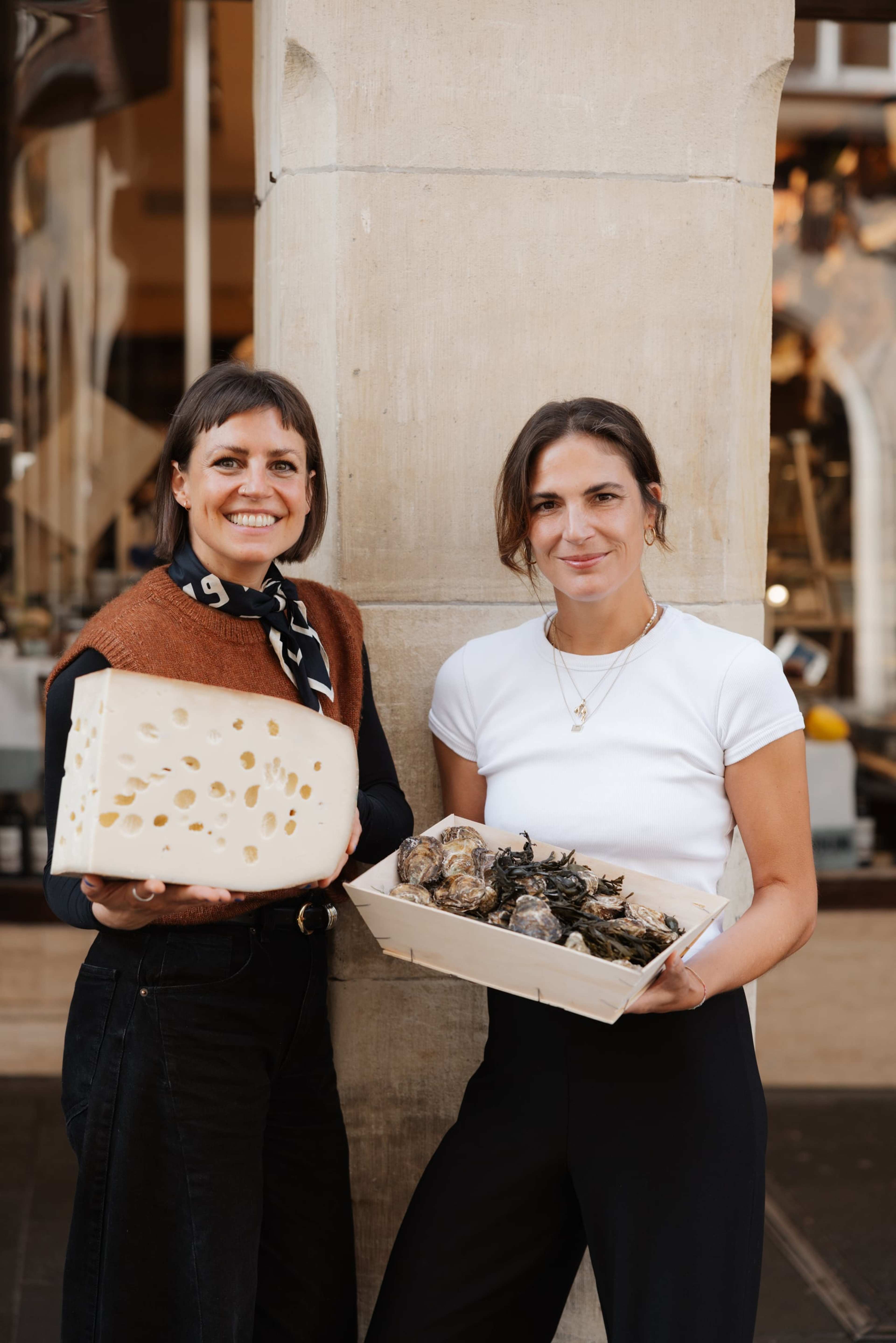 Judith und Sophie Helmrich an der Säule vor der Butterhandlung, die eine mit einem großen Stück Käse, die andere mit einer Kiste Austern